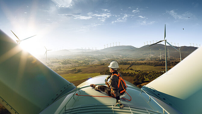 Ingénieur debout au sommet d'une éolienne et regardant un magnifique paysage au coucher du soleil.