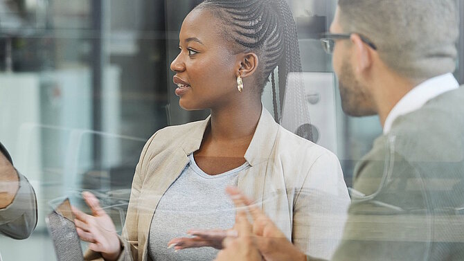 Behind a pane of glass, a woman and a man discuss business topics at a table