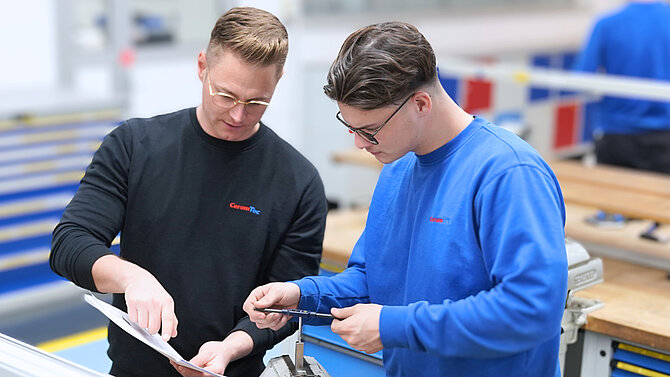 Two CeramTec employees discuss a workpiece made of high-performance ceramics in production.